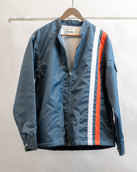 Racing Jacket 25 - Le Mans on wooden hanger, hanging from the top of the frame in front of white wall with tape in background.