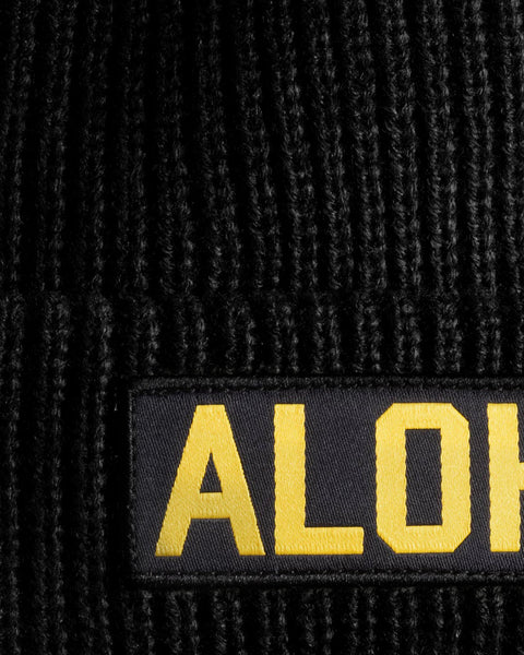 Closeup detail of black beanie with Aloha patch in yellow.