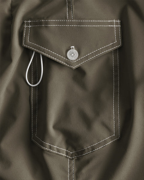 Close-up of the 806 SurfStretch Side Pocket Boardshorts - Army, showing the olive green pocket with white stitching, a flap secured by a silver snap button, and a white cord loop partially tucked under the flap.