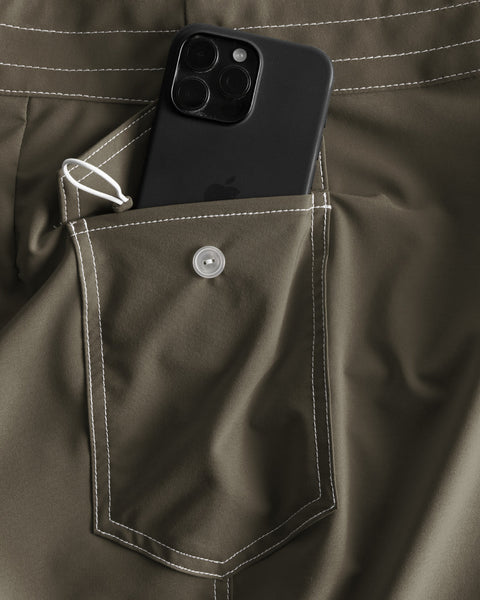 A close-up of the army green side pocket with white stitching on 806 SurfStretch Side Pocket Boardshorts, featuring a button flap, small white loop, and holding a triple-camera black smartphone—crafted for comfort and durability.