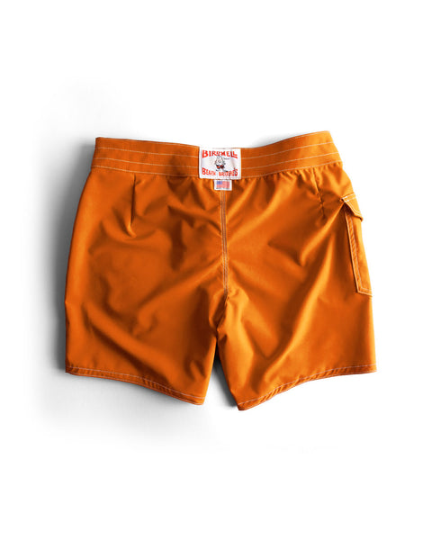 The 806 SurfStretch Side Pocket Boardshorts in medium orange feature a white waistband tag reading Birdwell in red, a back pocket with flap, visible stitching, and are made in the USA. Shown laid flat on a white background.