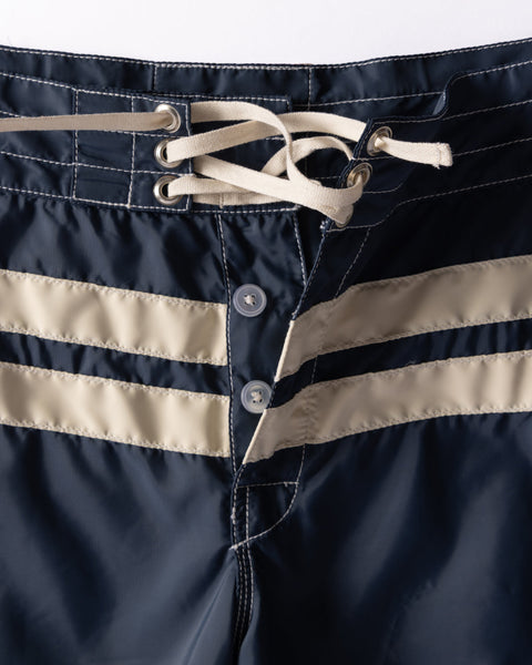 Close-up of the waistband of the 300 Comp Stripe - Navy/Bone boardshorts, showing two beige stripes, lace-up drawstring with metal eyelets, and button fly closure.