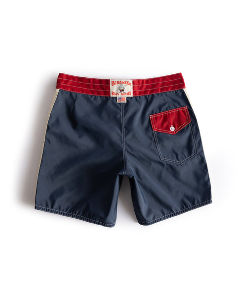 The 300 Legend boardshorts in Navy/Red/Bone feature a red waistband, red and white buttoned back pocket, label on the waistband, and white side stripes. Shown laid flat on a white background.